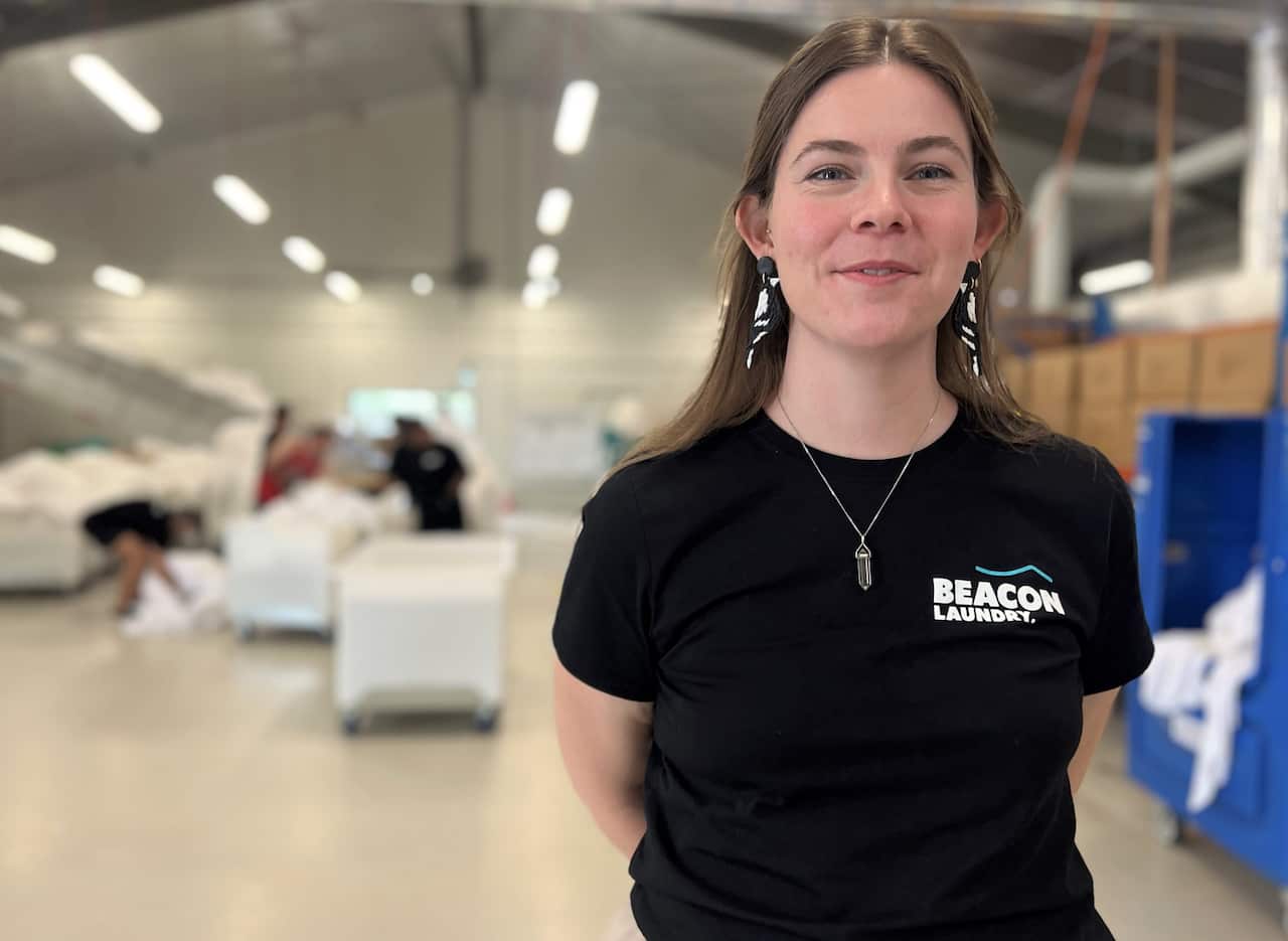 A woman in a black t-shirt stands in a commercial laundry.