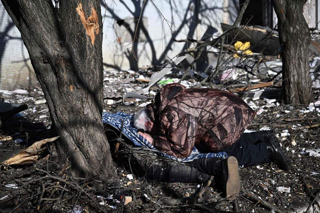 A man reacts at the body of a relative outside a destroyed building on the eastern town of Chuguiv, February 24, 2022