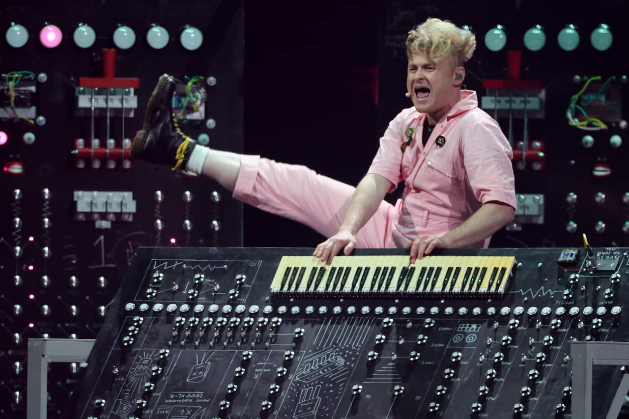 A singer raises his right leg as he performs at a stage playing a keyboard