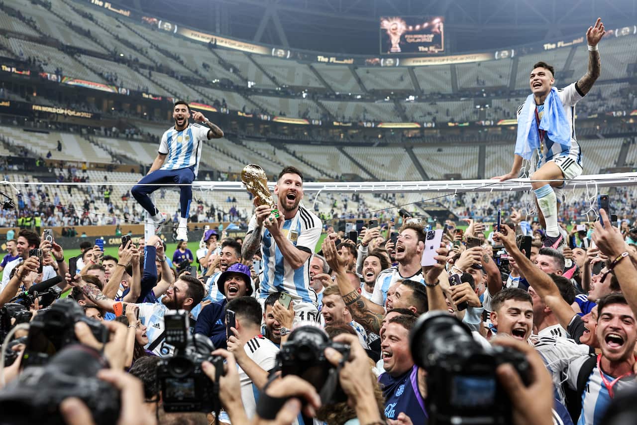 Argentina captain Lionel Messi (C midground), teammates and fans celebrate with the trophy after the trophy ceremony for the 2022 FIFA World Cup final football match between Argentina and France at Lusail Iconic Stadium. Argentina won 3-3 (4-2) in a penalty shootout. 