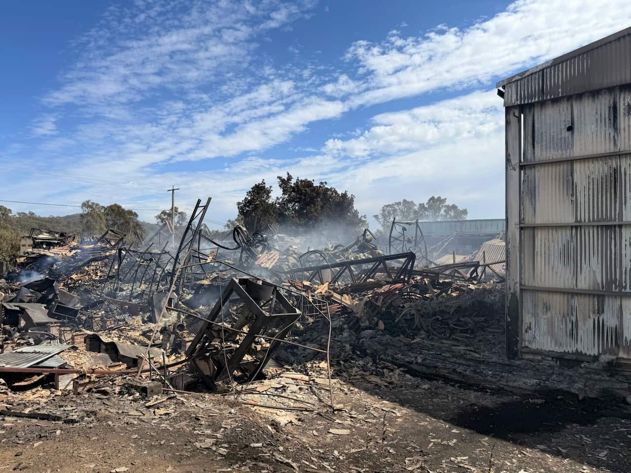 A burned out building with debris still smoking after a bush fire.