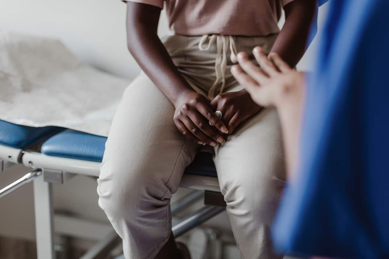 Healthcare worker talking to a female patient sitting on a hospital bed. 