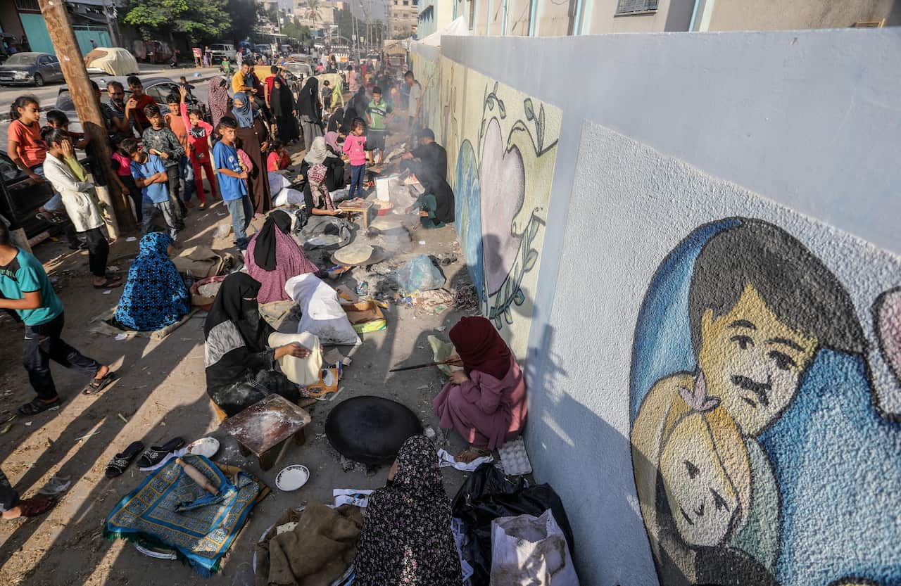 Palestinian women bake traditional saj bread over a wood fire and paper in a school yard.