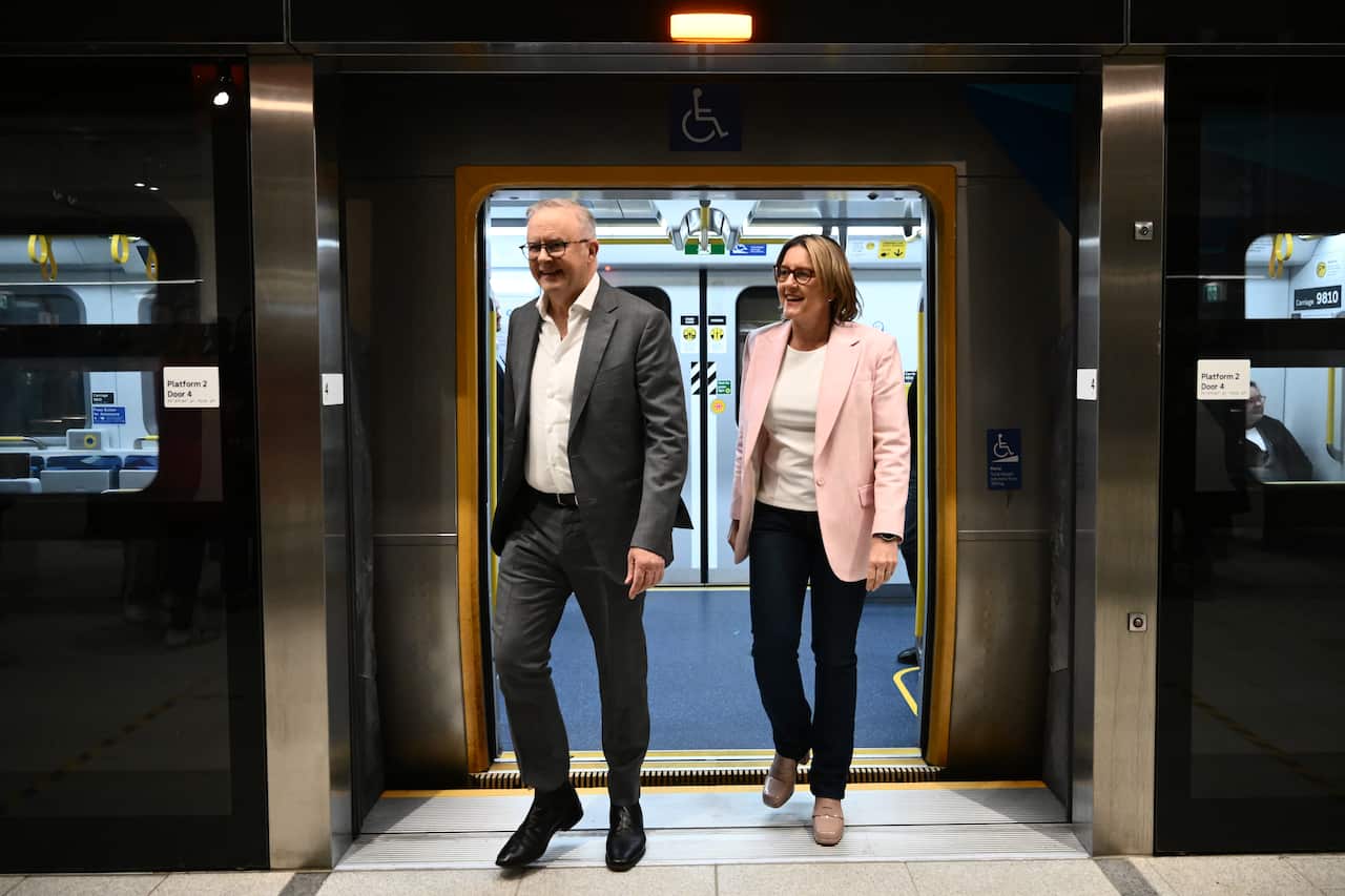 A man dressed in a suit walks off a train along with a woman.