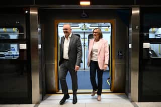 A man dressed in a suit walks off a train along with a woman.