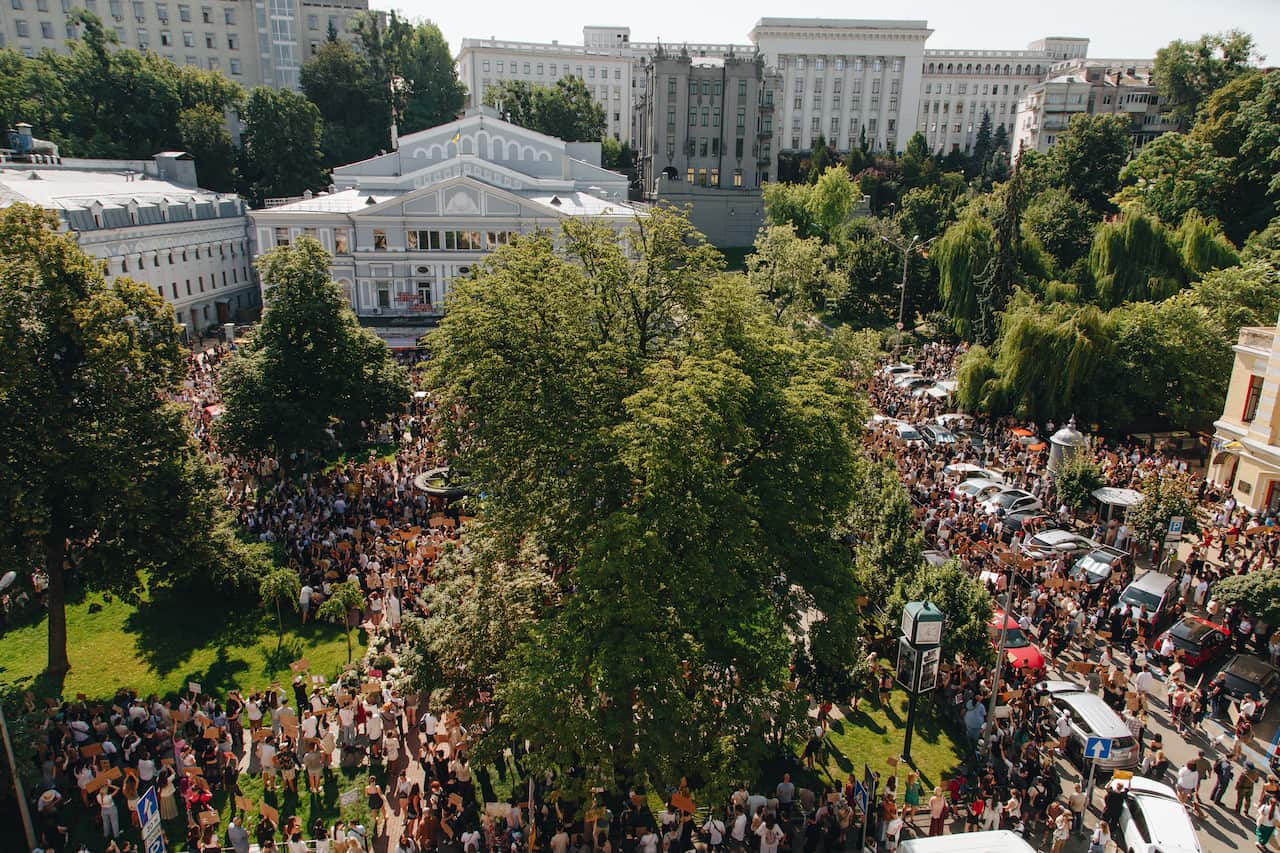 A large crowd of protesters in a park area outside a government building.
