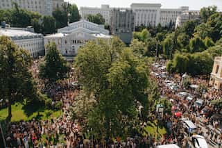 A large crowd of protesters in a park area outside a government building.