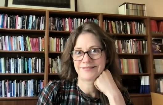 A woman on a video call. Behind are shelves full of books.