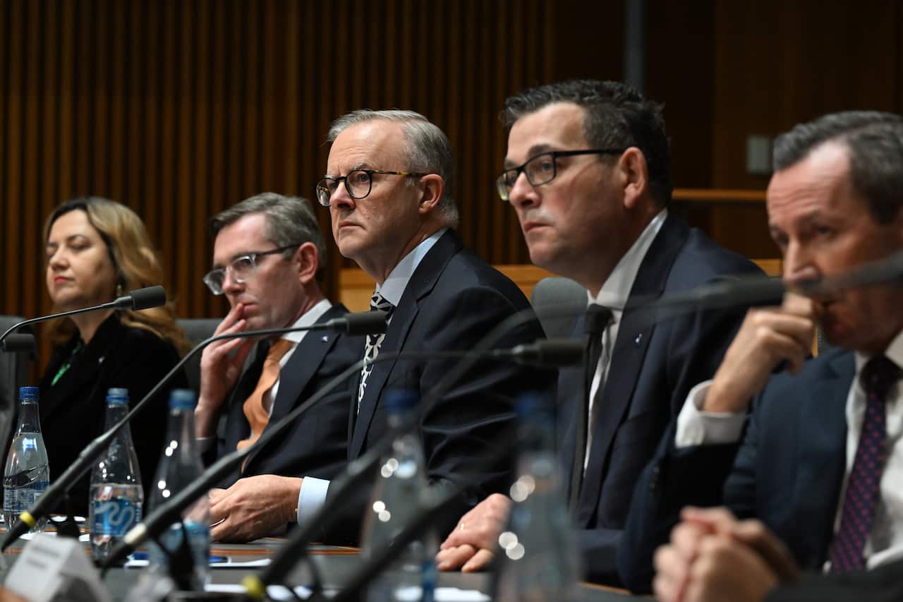 Four men in suits and one woman sit near microphones.
