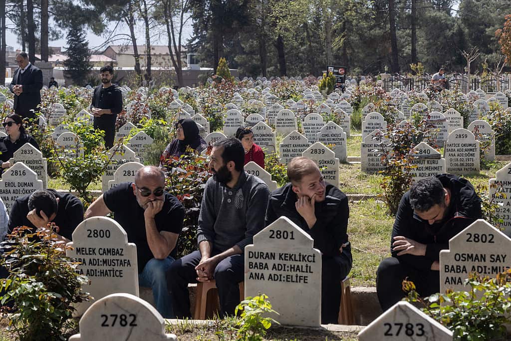 Mourners sit among grave stones in a field.