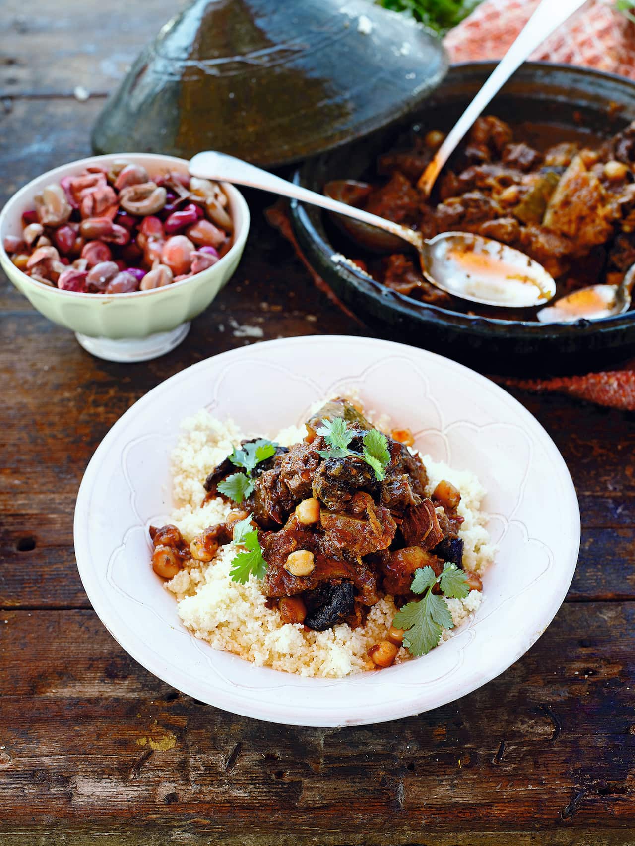 A white bowl with couscous and rich beef stew sits beside a tagine.