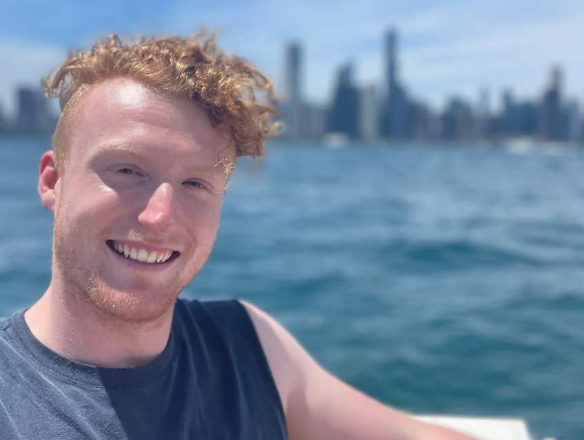 Jack smiles in a selfie taken overlooking a city water view. 
