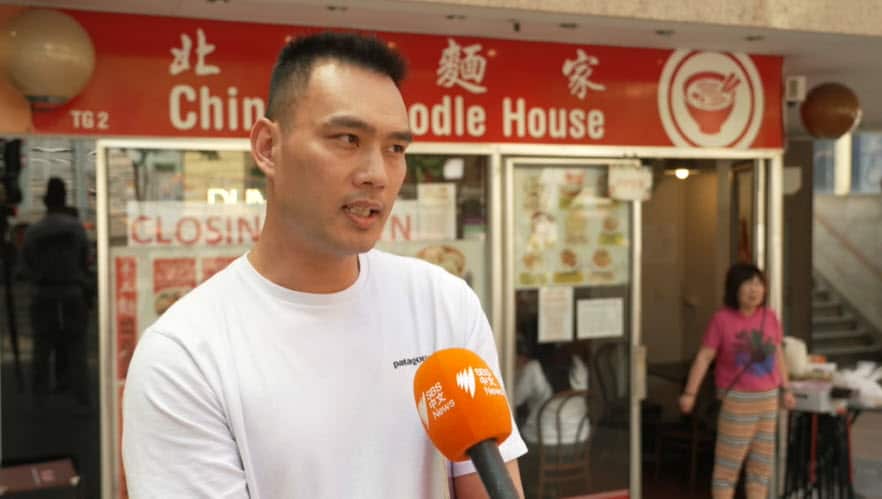 A man in a white shirt speaking into an orange microphone.