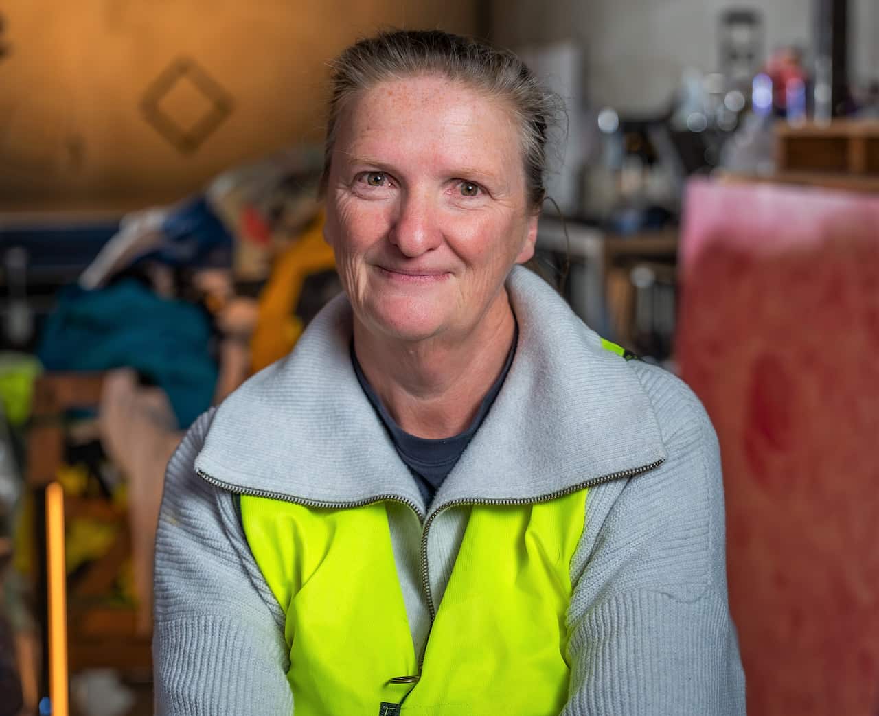 A woman in a hi-viz vest sits in a warehouse looking at camera. 