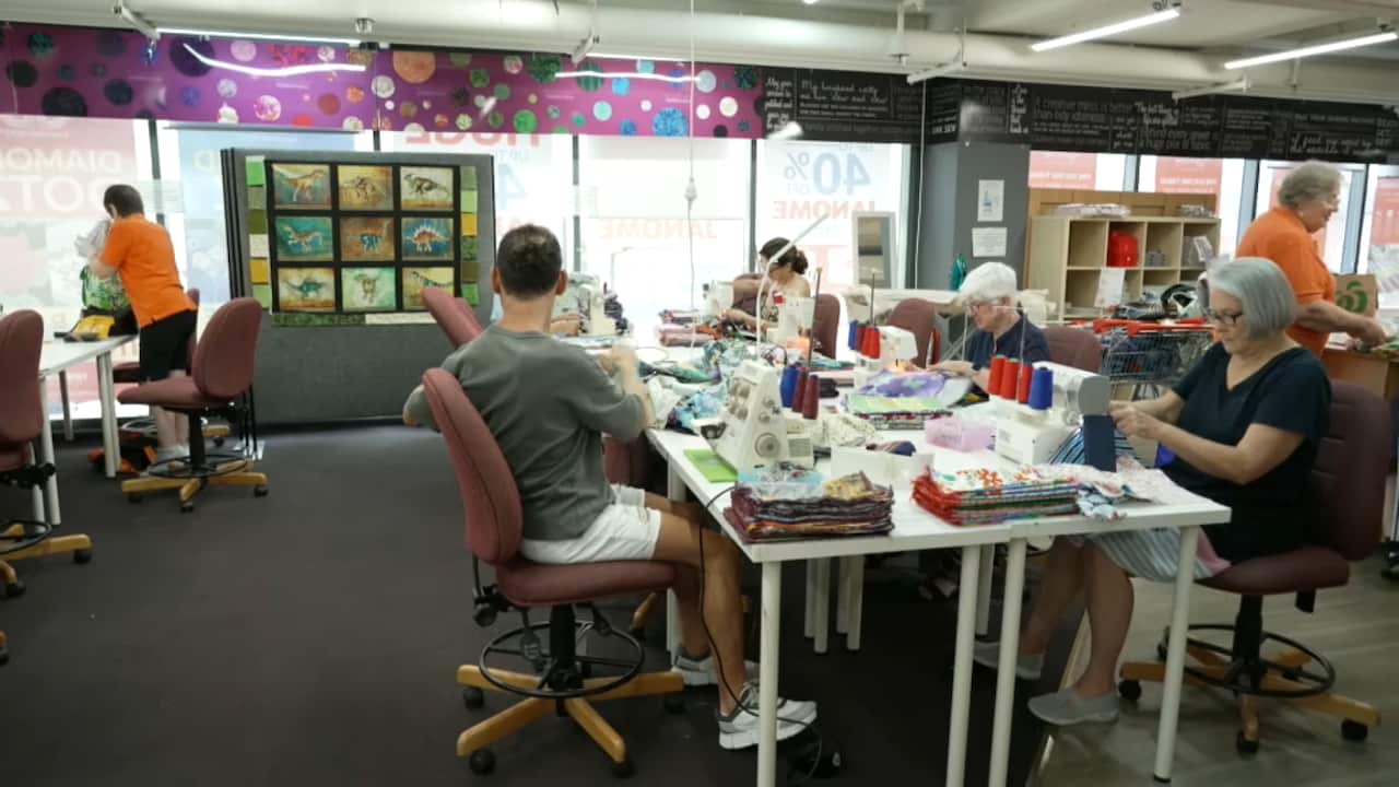 A group of people sit along a table with sewing machines in front of them.