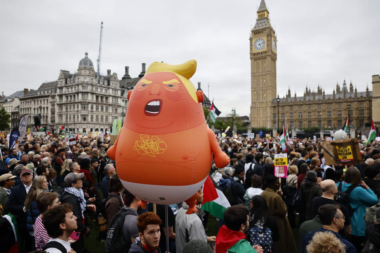 A large crowd of protesters, one of whom is holding up a balloon that resembles Donald Trump.