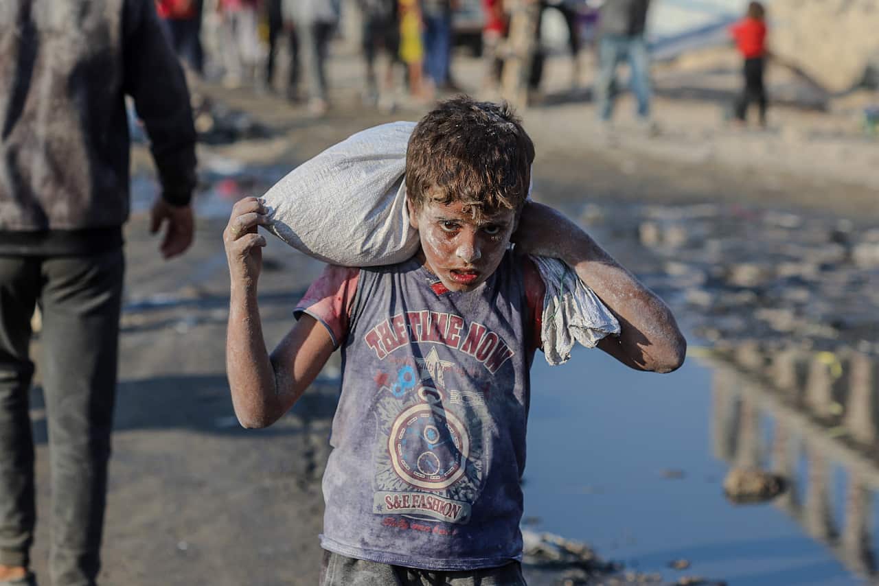 A boy carrying white sack across his shoulder