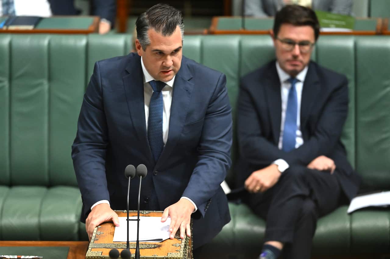  A man in a suit and tie standing a speaking inside 