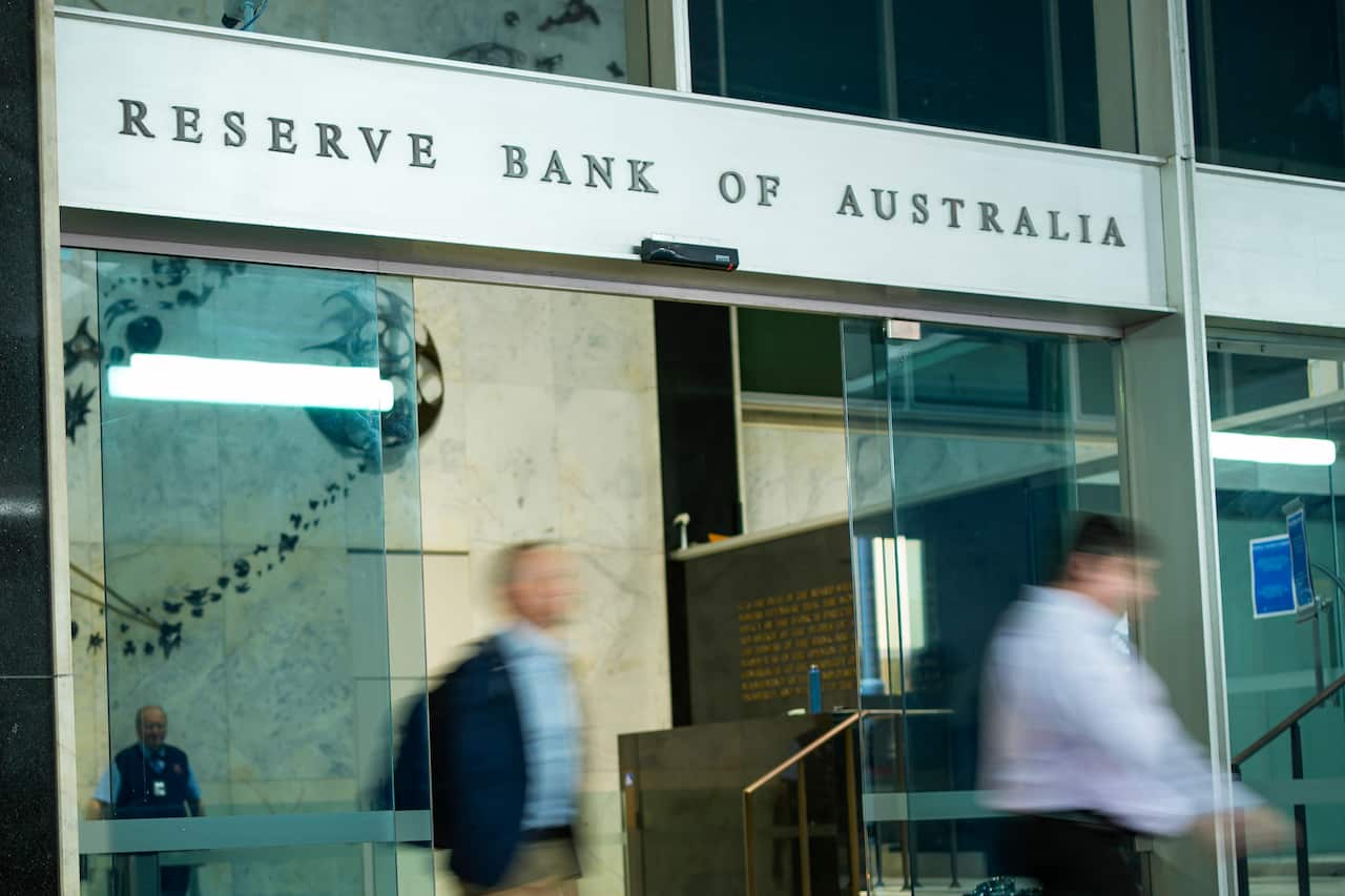 Blurry figures in the foreground walk through the doors of the Reserve Bank.
