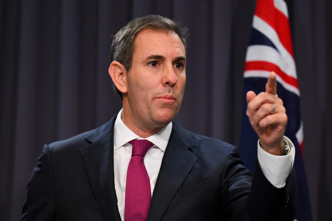 A man in a suit and tie raises his left hand as he speaks at a presser.