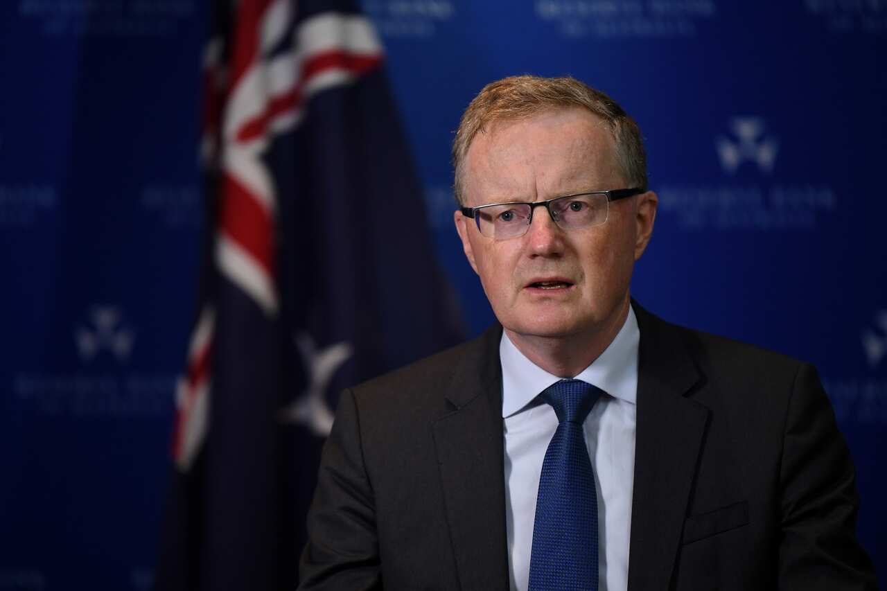 A man wearing a suit and tie speaking in front of an Australian flag.