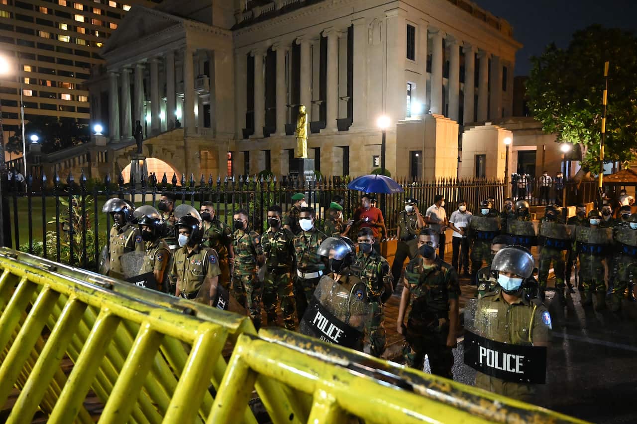 Anti-riot police are seen standing in position behind a fence as they face protestors.