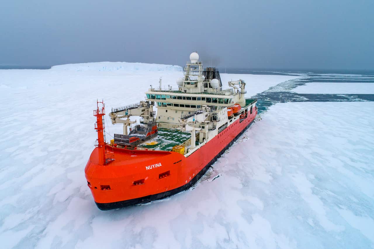A large, red-coloured ship sails through icy waters.