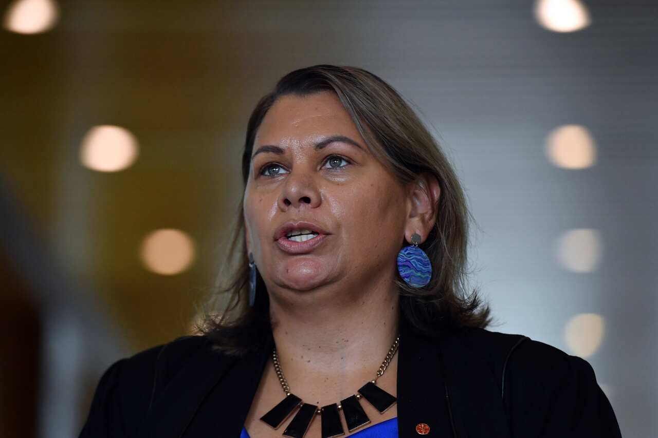 A head shot of Dorinda cox in a black blazer, blue blouse and blue earrings mid-speech