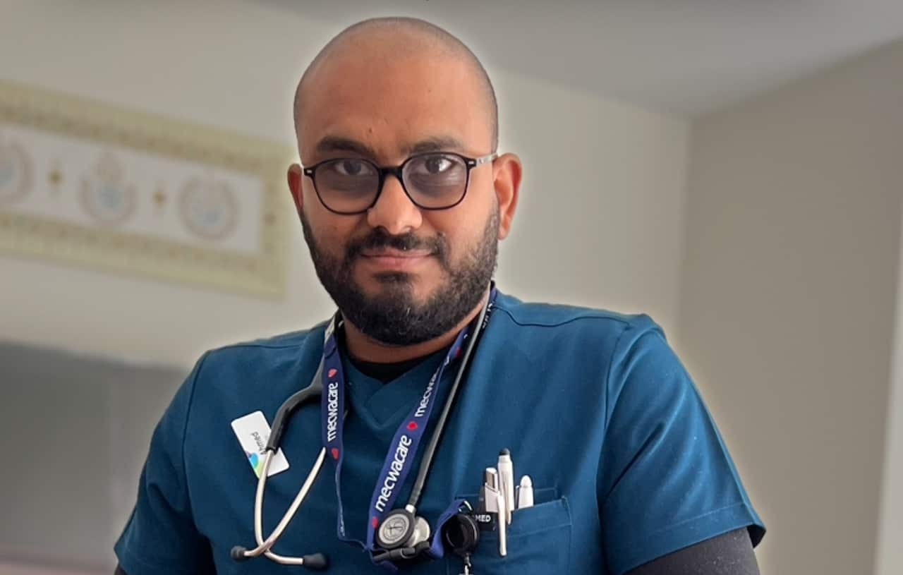 A man wearing doctor's scrubs and with a lanyard and a stethoscope around his neck