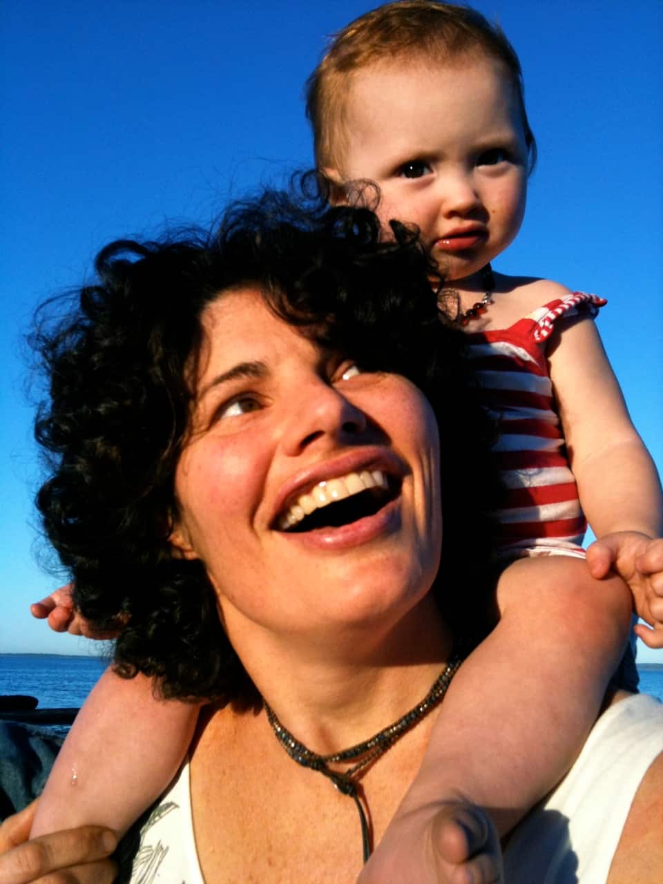 A smiling mother carries her happy toddler on her shoulders.