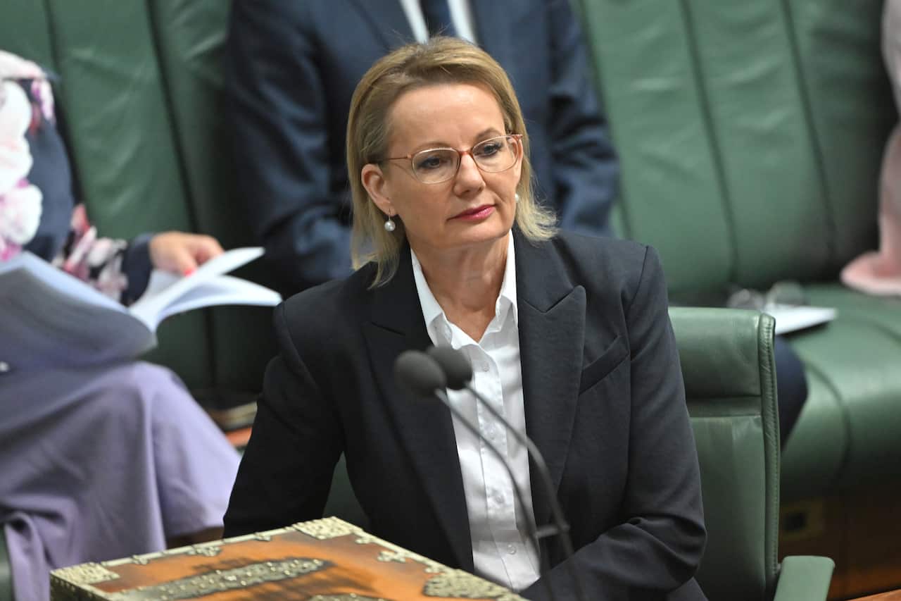 A middle-aged white woman with blonde hair, wearing glasses, a blazer and white shirt. 
