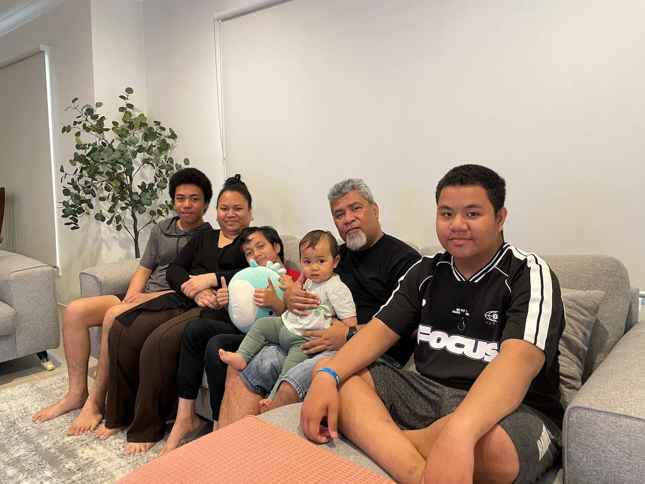 The Manuella family sit in the living room, smiling to the camera