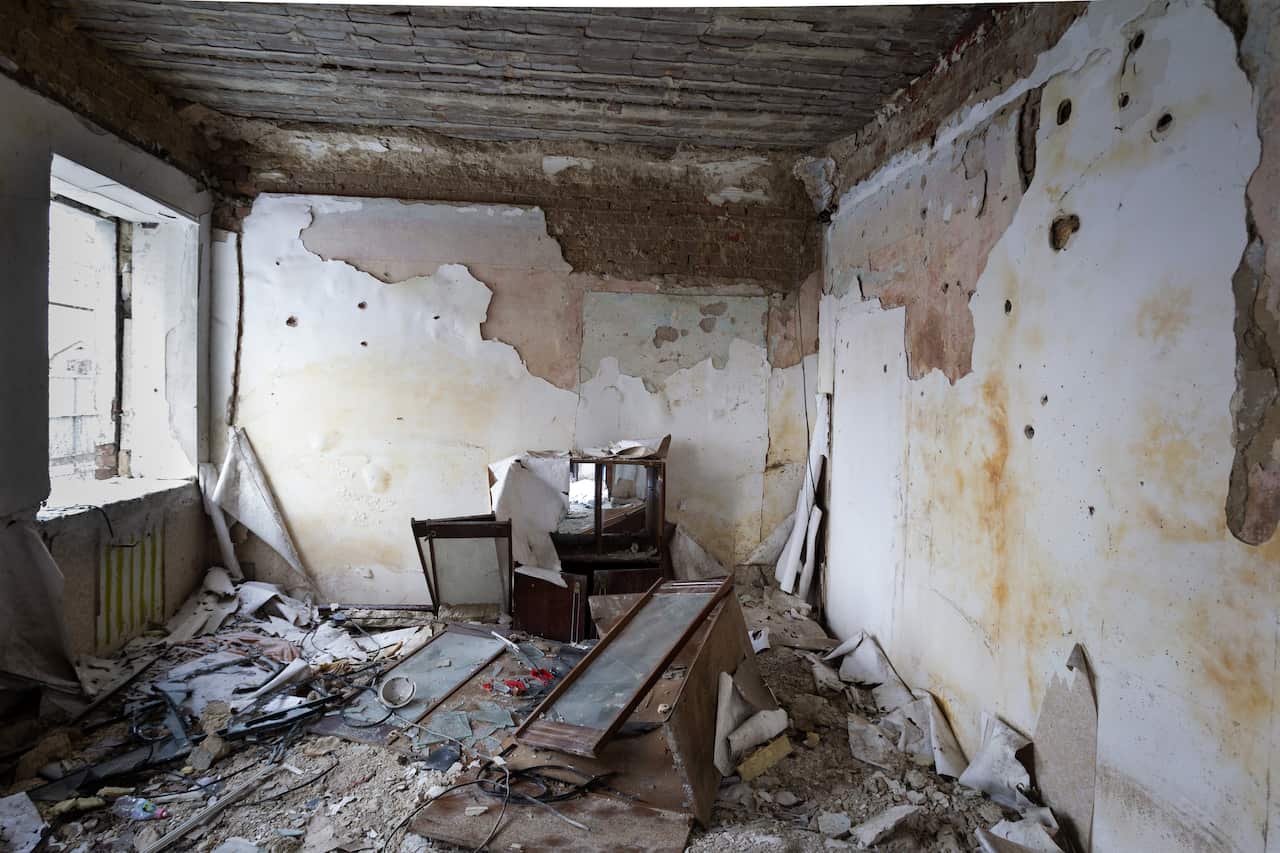 A destroyed room with dirty walls, broken furniture and window panes scattered on the floor.