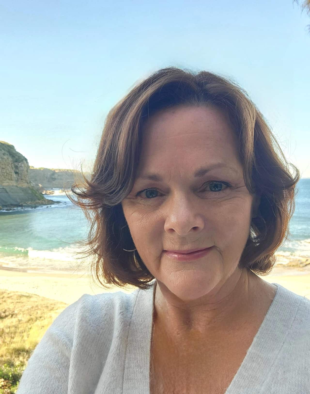 A woman with a neutral expression with the ocean in the background.