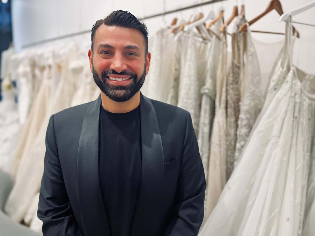 A man with a rack of wedding dresses behind him
