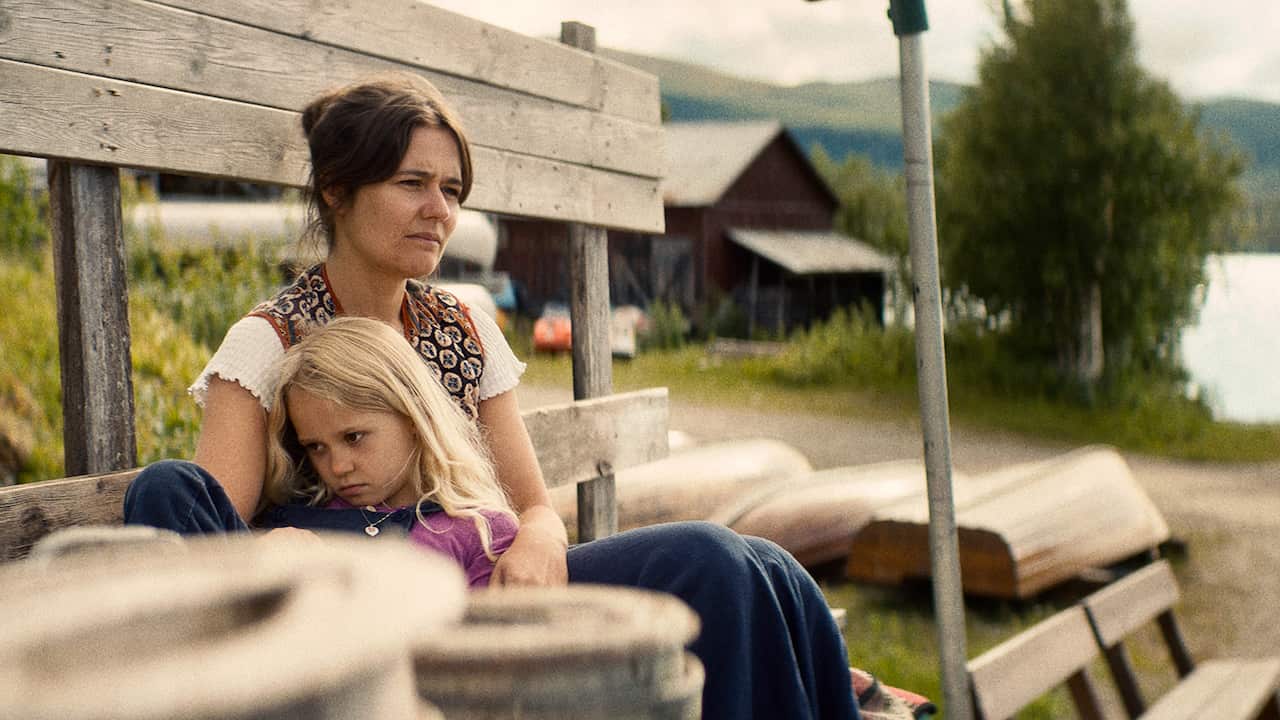 A woman and a worried little girl sit on a bench near a river. 
