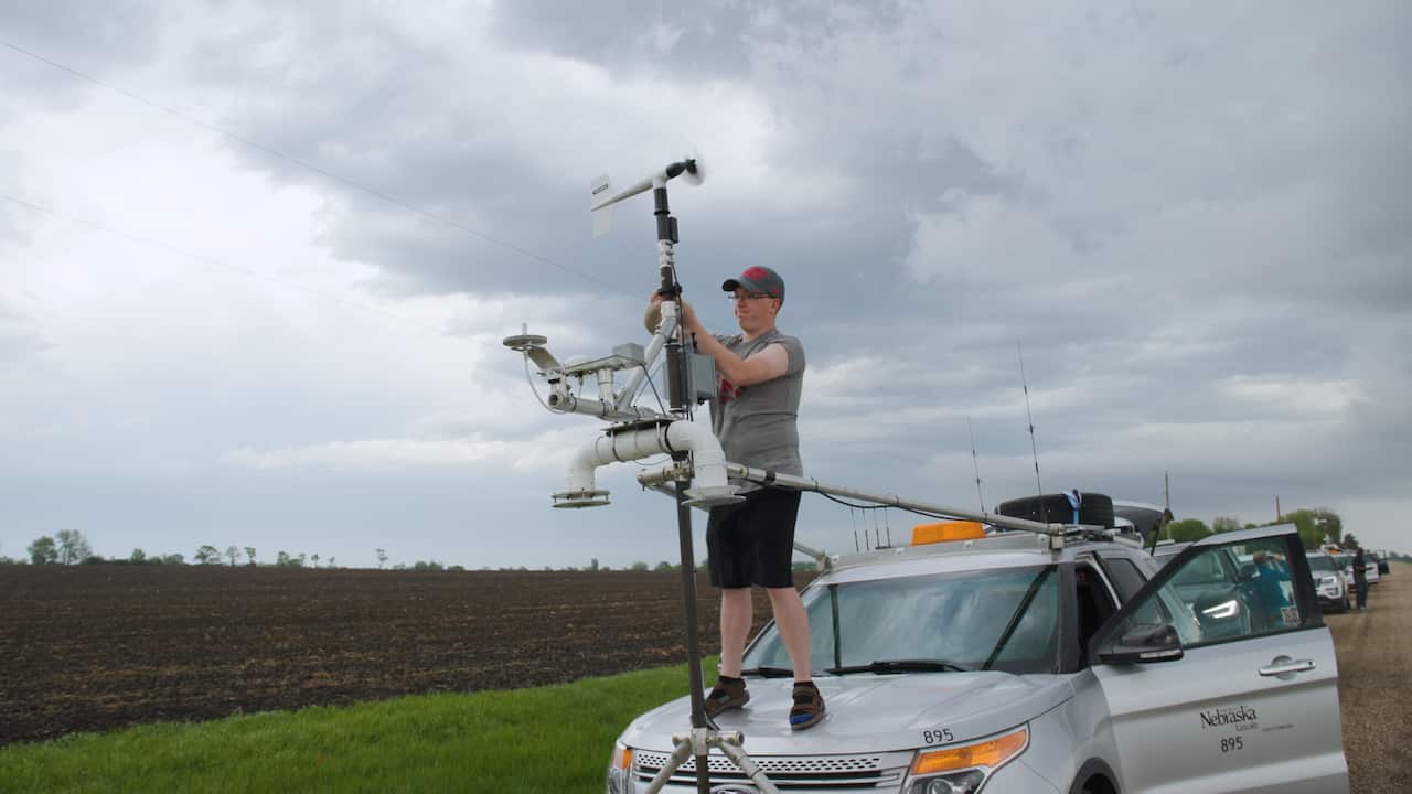 A young man stands on the front of a car. 