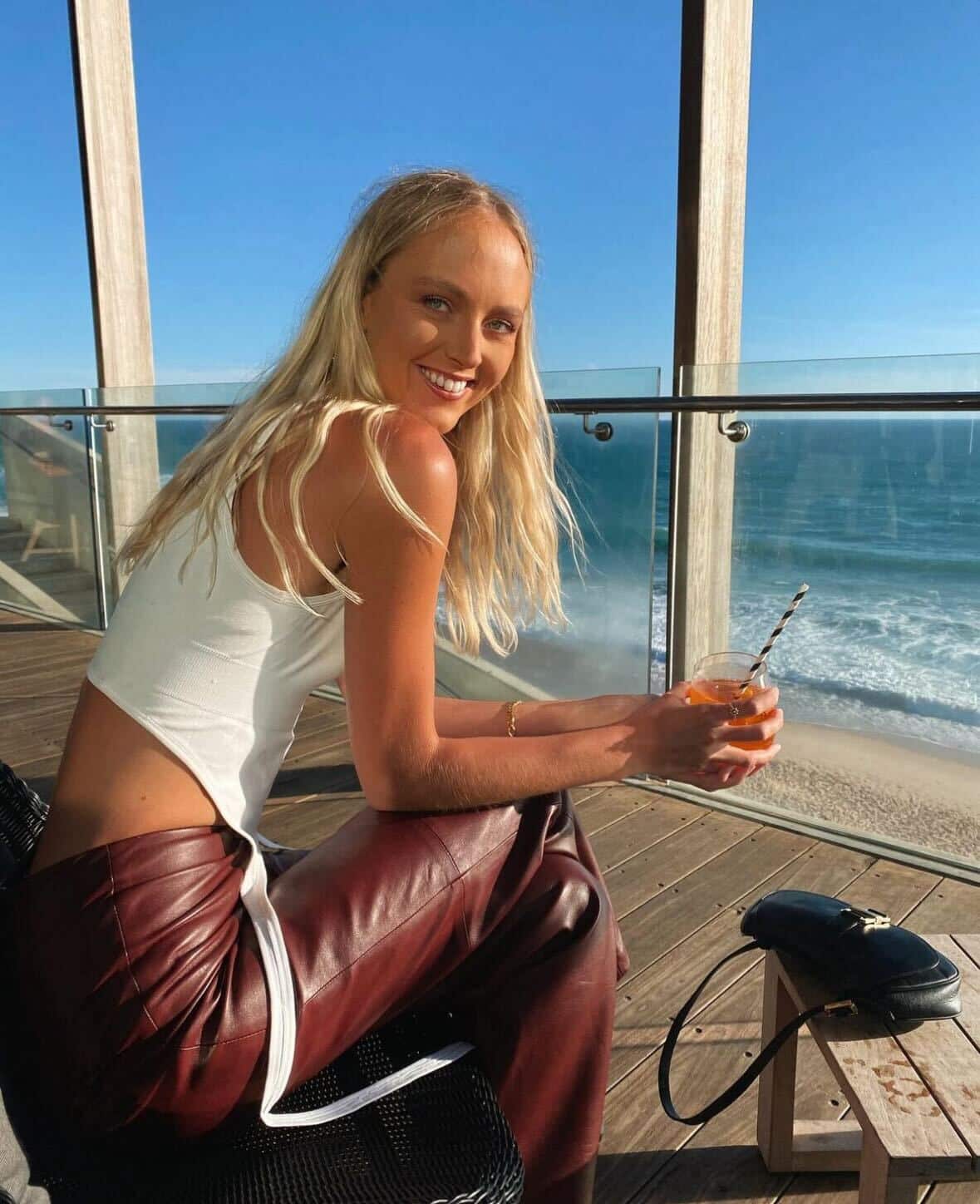 A young woman sitting on balcony by the ocean holding a drink. 
