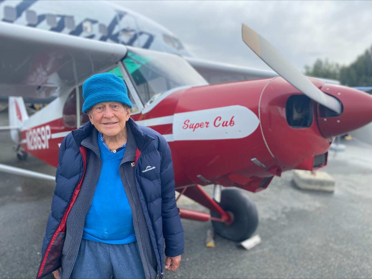 An elderly man standing in front of a plane. 