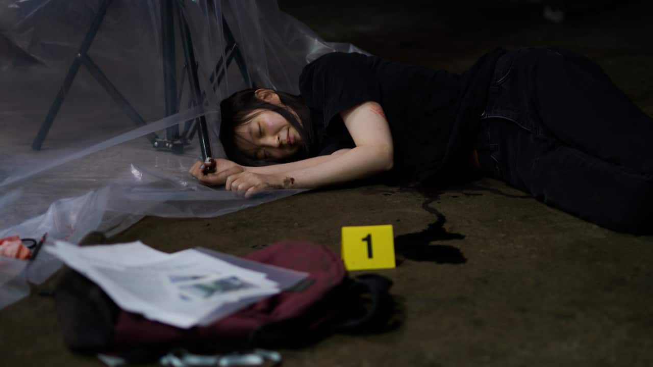 A young woman lies on the floor in a make-shift crime scene pretending to be dead.