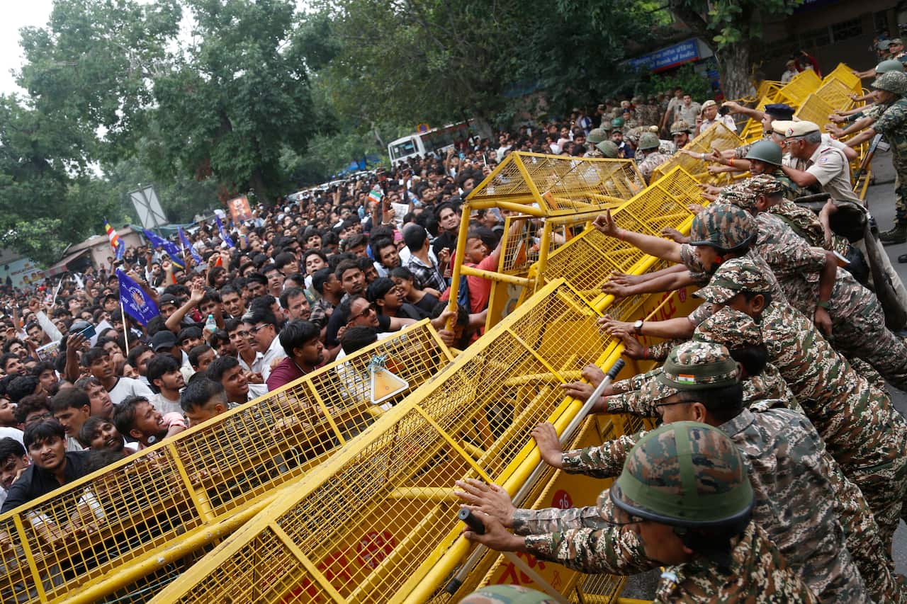 A crowd try to push through yellow barricades with police personnel trying to push from the opposite side