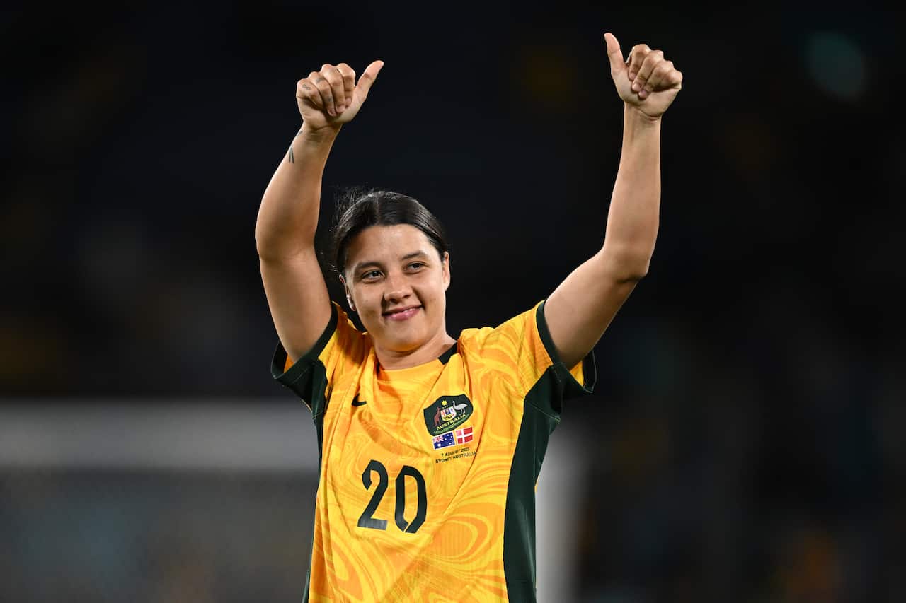 A woman in a yellow shirt raises two thumbs up.