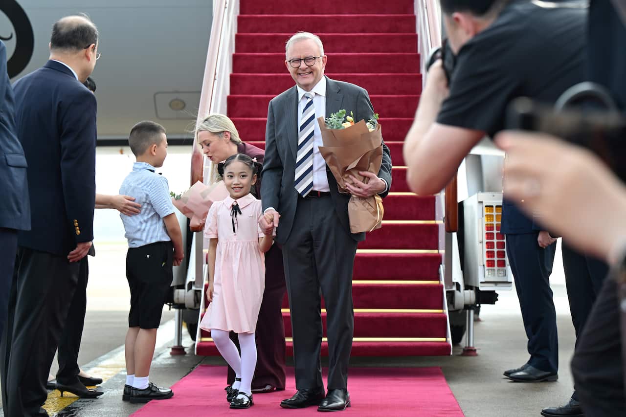 Anthony Albanese holds the hand of a young Chinese girl in front of a plane with steps