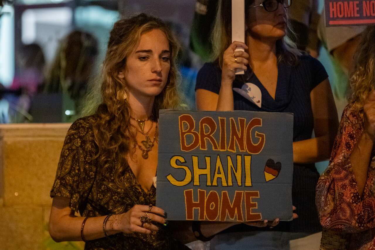 A woman holds up a placard that says "Bring Shani Home".
