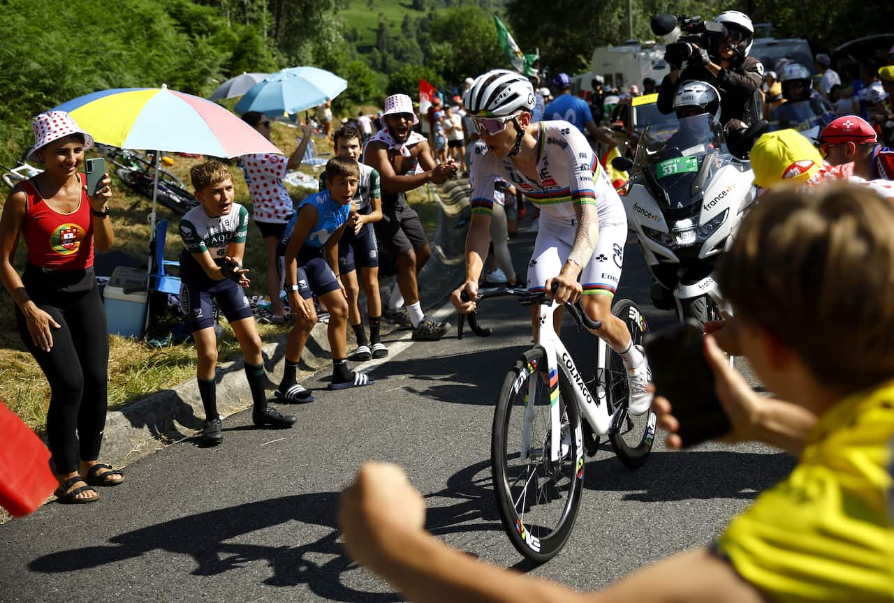A cyclist in a white cycling hit is being cheered on by fans as he rides along a road.