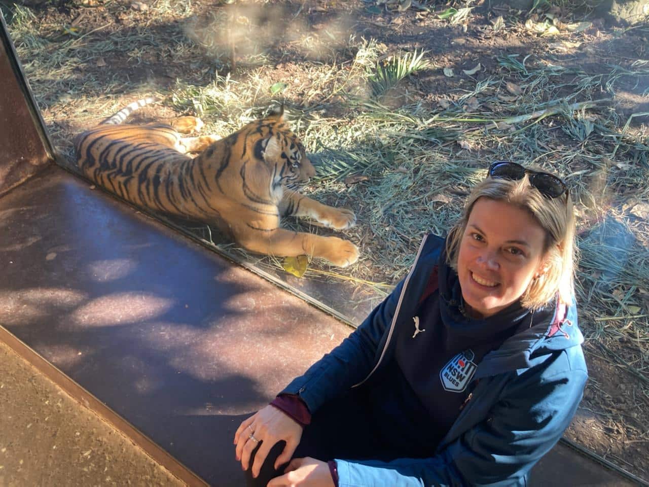 Leigh-Anne sitting next to a tiger in zoo. 