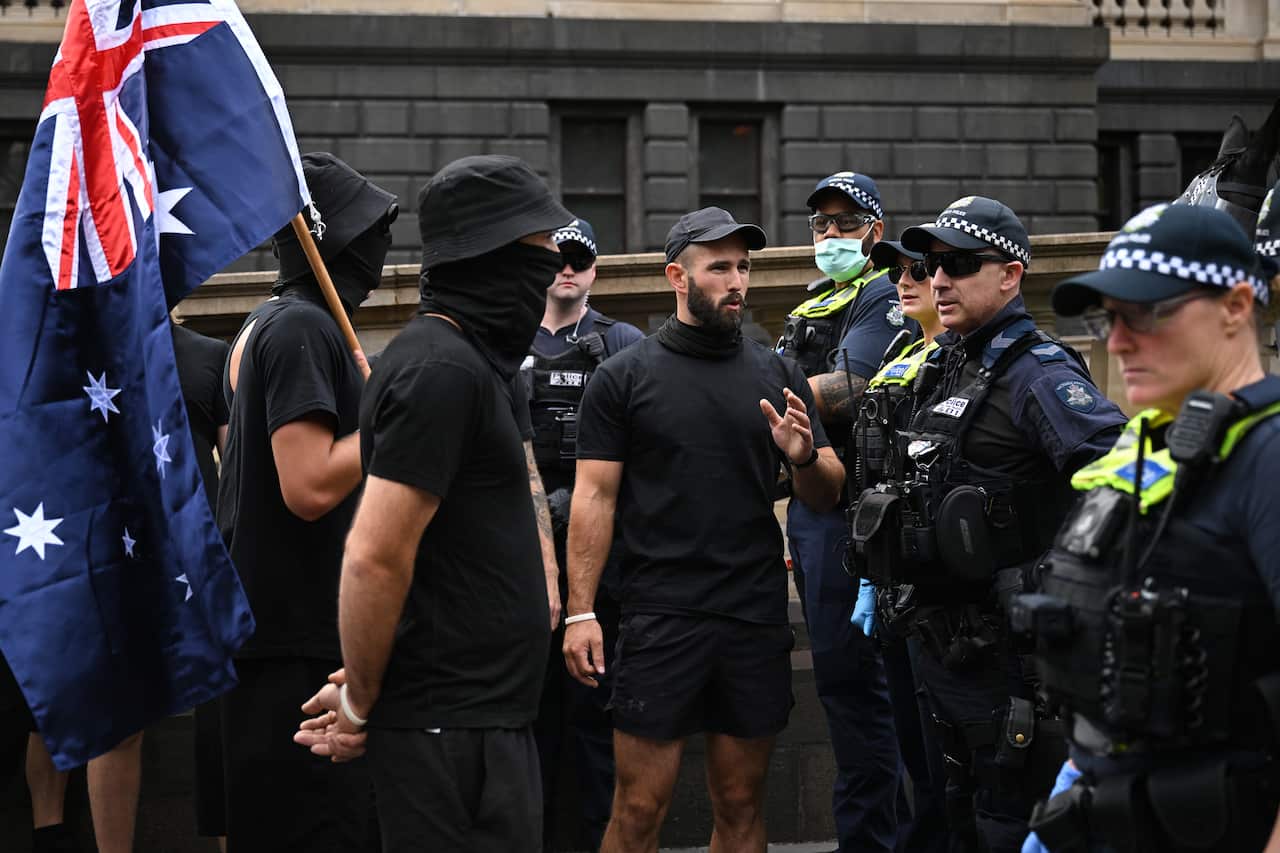 A group of mean wearing black standing in front of police officers.