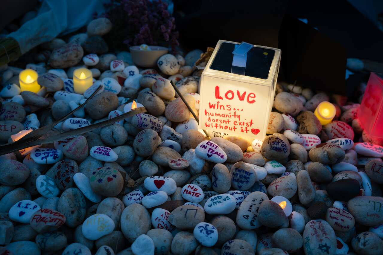 Pebbles with messages including "RIP" and "NO HATE", illuminated by a small light box that says "Love wins". 