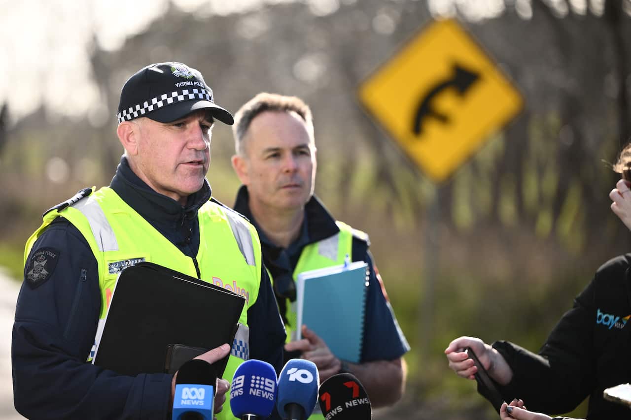 Two men speak to reporters on a highway. 