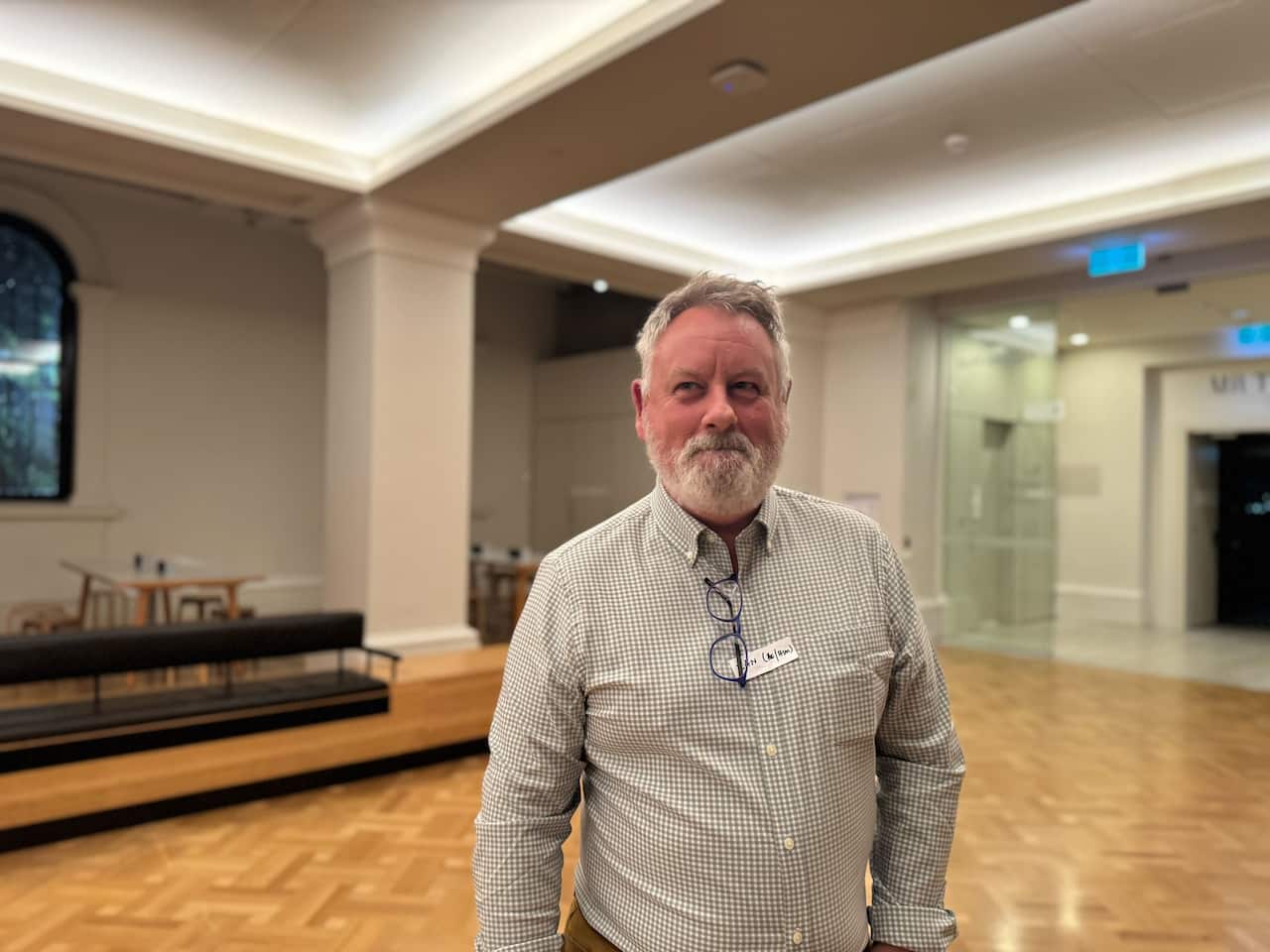 An older man wearing a button-up shirt smiling inside a room.